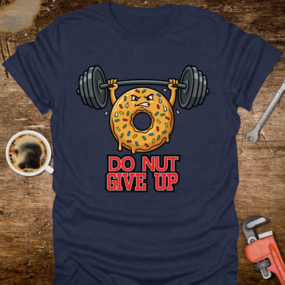 Navy blue t-shirt with a donut lifting weights graphic and 'Do Nut Give Up' text on a wooden surface with coffee and tools.