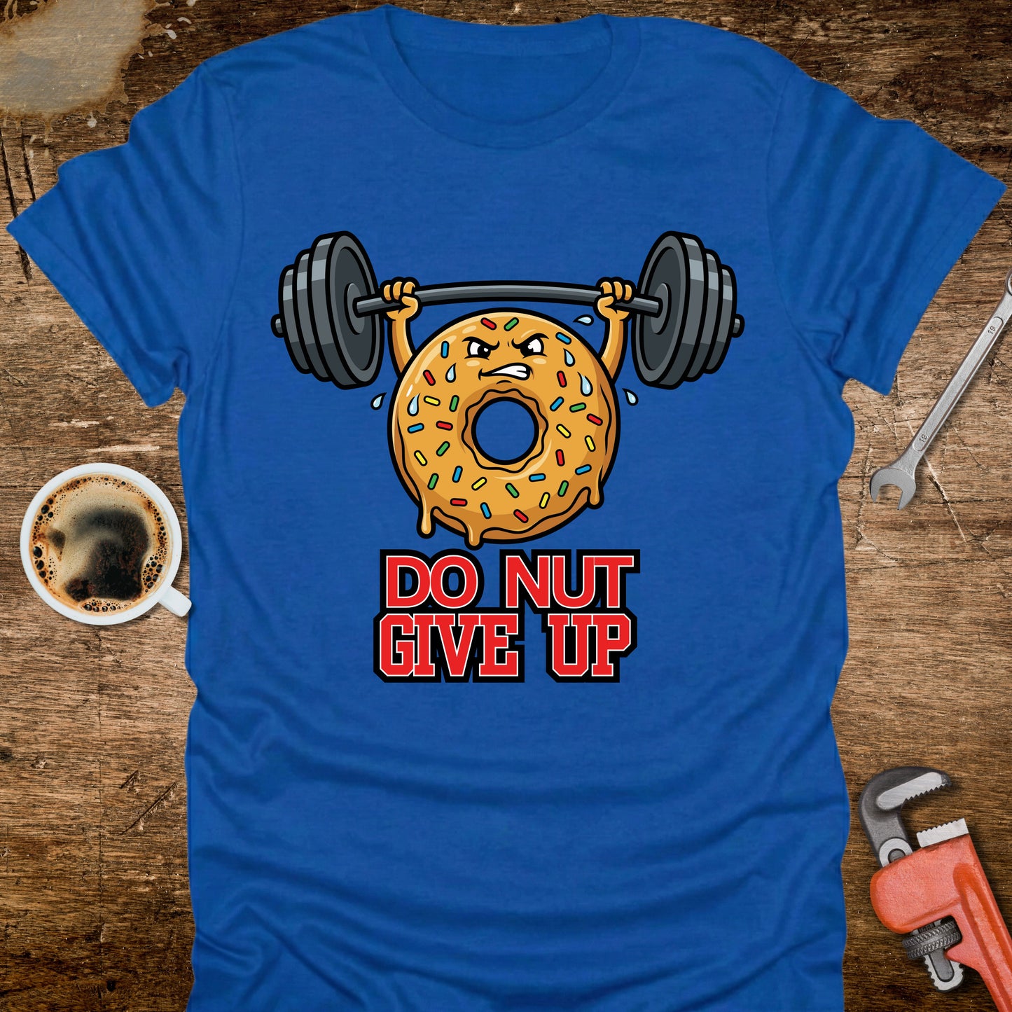 Blue t-shirt with a donut lifting weights graphic and 'DO NUT GIVE UP' text on a wooden surface.