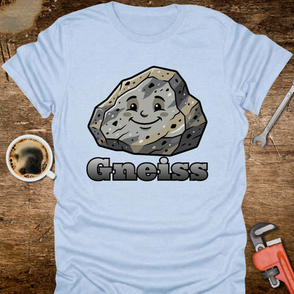 Light blue t-shirt with a cartoon gneiss rock and 'Gneiss' text on a wooden surface with tools and a coffee cup.
