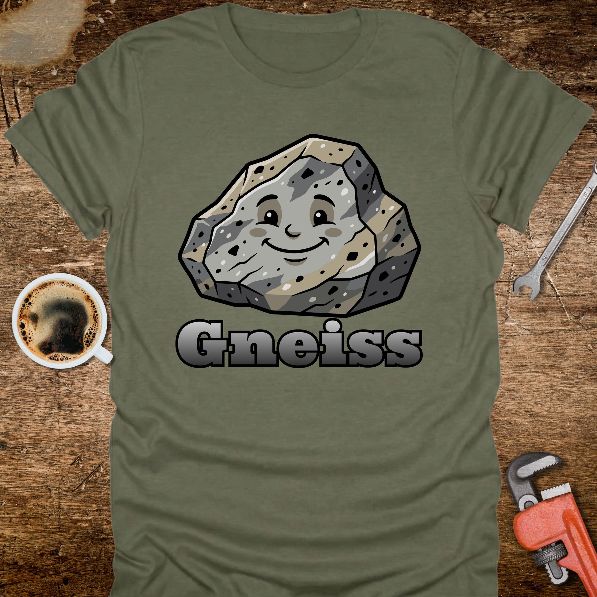 Green t-shirt with a smiling gneiss rock graphic and 'Gneiss' text on a wooden surface with coffee and tools.