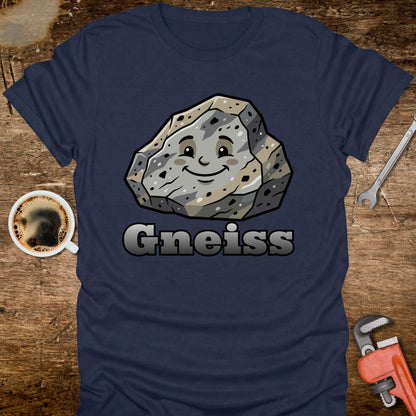Navy blue t-shirt with a cartoon gneiss stone graphic and 'Gneiss' text on a wooden surface with tools and coffee.