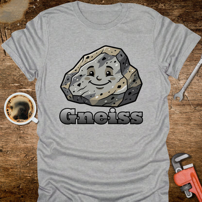 Gray t-shirt with a cartoon gneiss stone graphic and the word 'Gneiss' on a wooden surface with a coffee cup and tools.