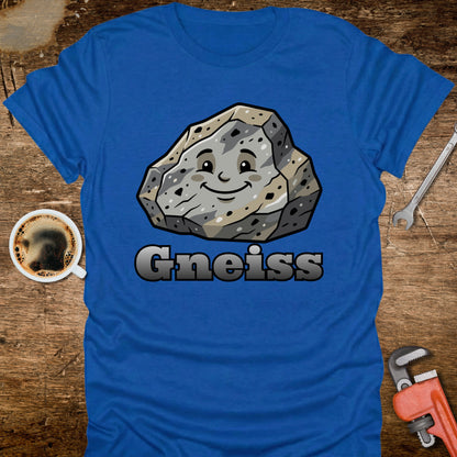 Blue t-shirt with a smiling gneiss rock graphic and 'Gneiss' text on a wooden surface with tools and a coffee cup.
