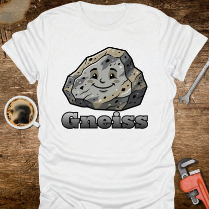 White t-shirt with a cartoon gneiss rock graphic and 'Gneiss' text on a wooden surface with tools and a coffee cup.