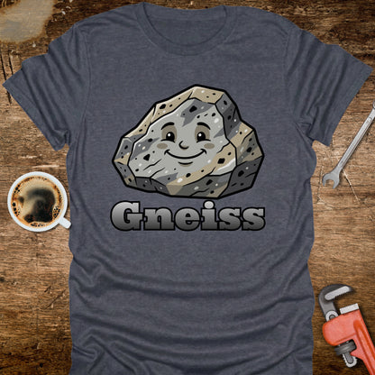Blue t-shirt with a cartoon gneiss stone graphic and the word 'Gneiss' on a wooden surface with a coffee cup and tools.
