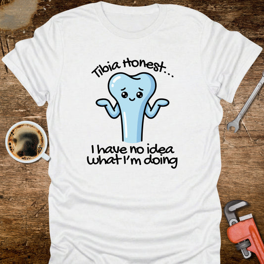 White t-shirt with a cartoon tooth graphic and text on a wooden surface with coffee and tools.