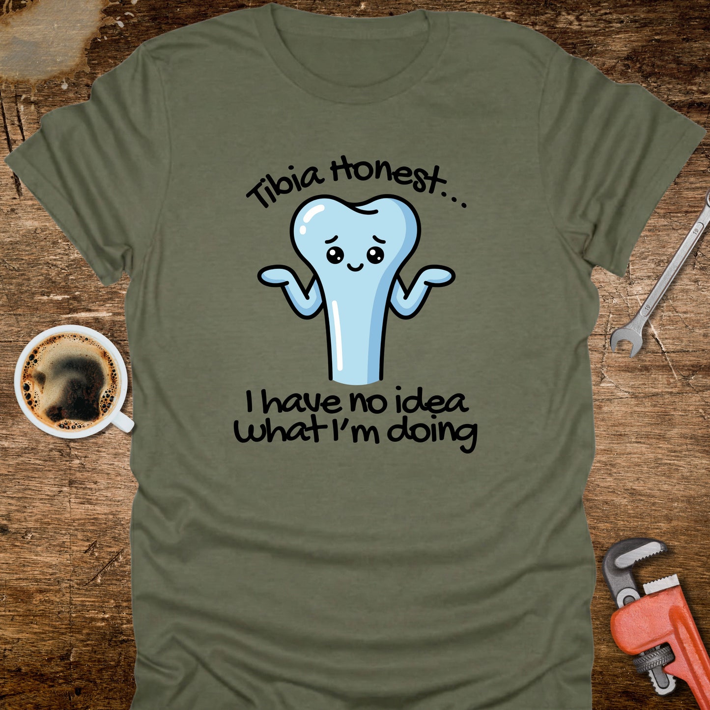 Green t-shirt with a cartoon tooth graphic and text on a wooden surface with coffee and tools.