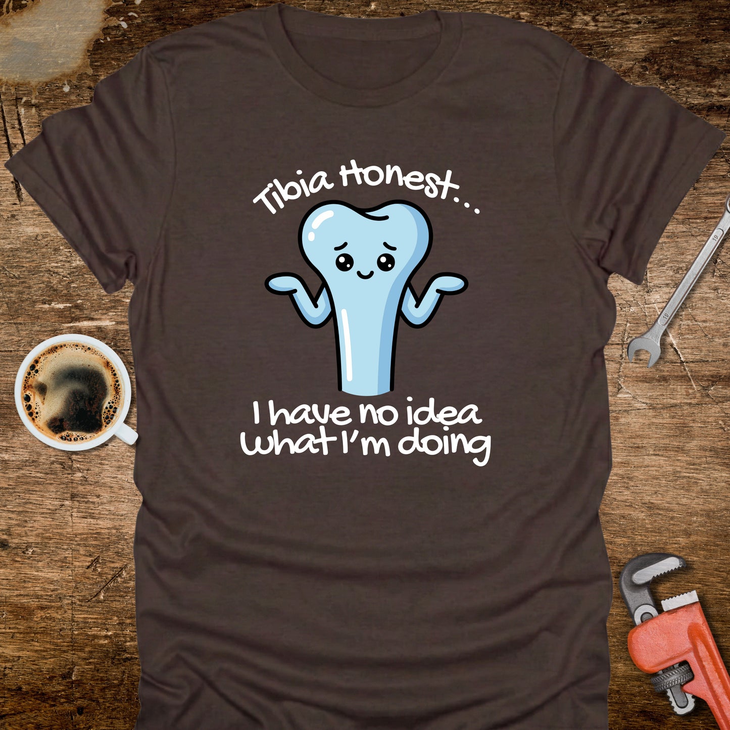 Brown t-shirt with a cartoon tooth graphic and text on a wooden surface with coffee and tools.