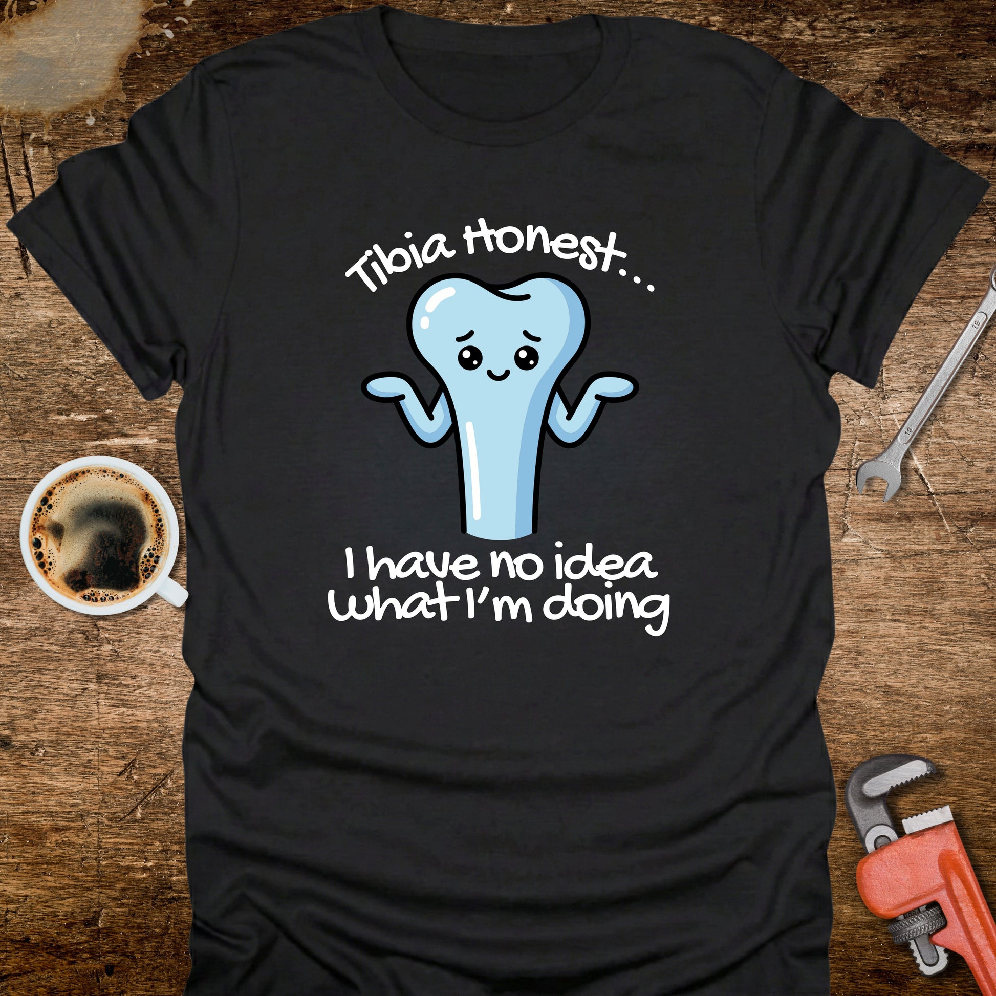 Black t-shirt with a cartoon tooth graphic and text on a wooden surface with a coffee cup and tools.
