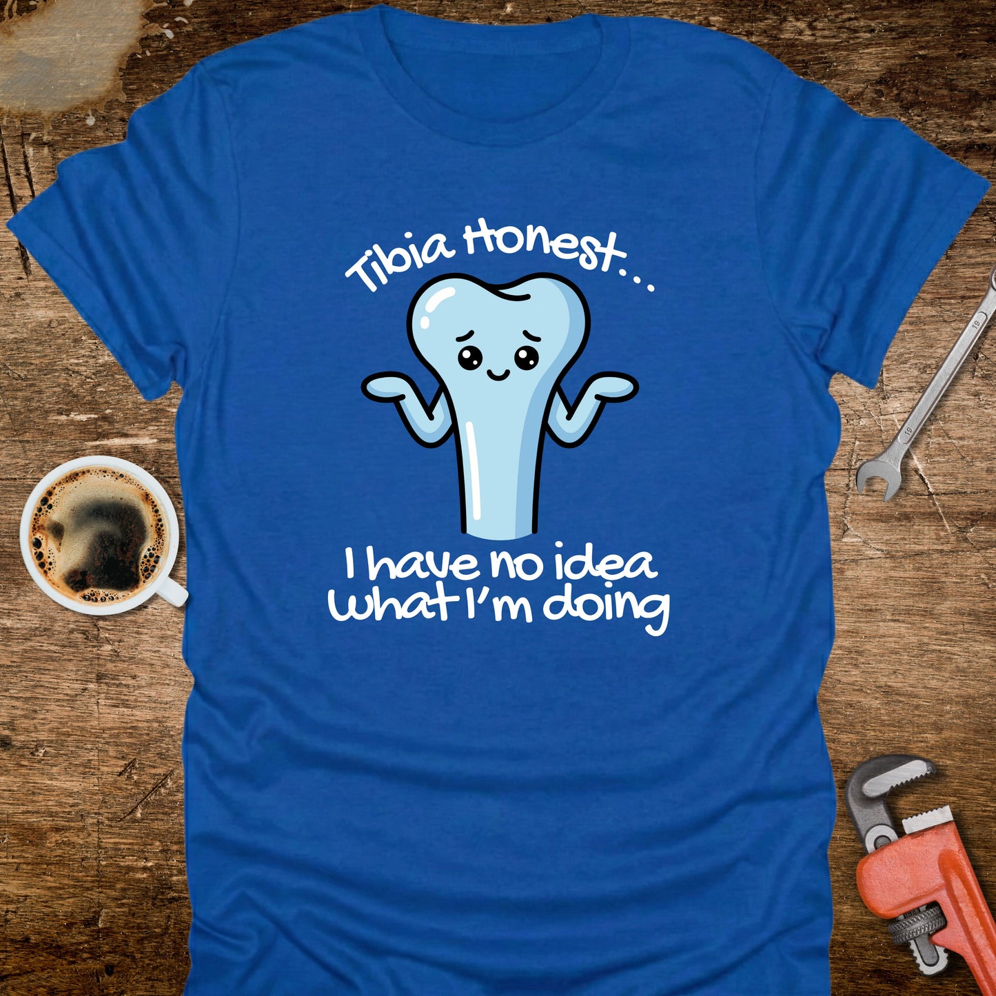 Blue t-shirt with a cartoon tooth graphic and text on a wooden surface with a coffee cup and tools.