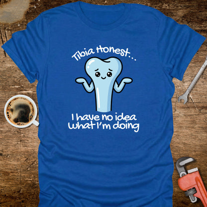 Blue t-shirt with a cartoon tooth graphic and text on a wooden surface with a coffee cup and tools.