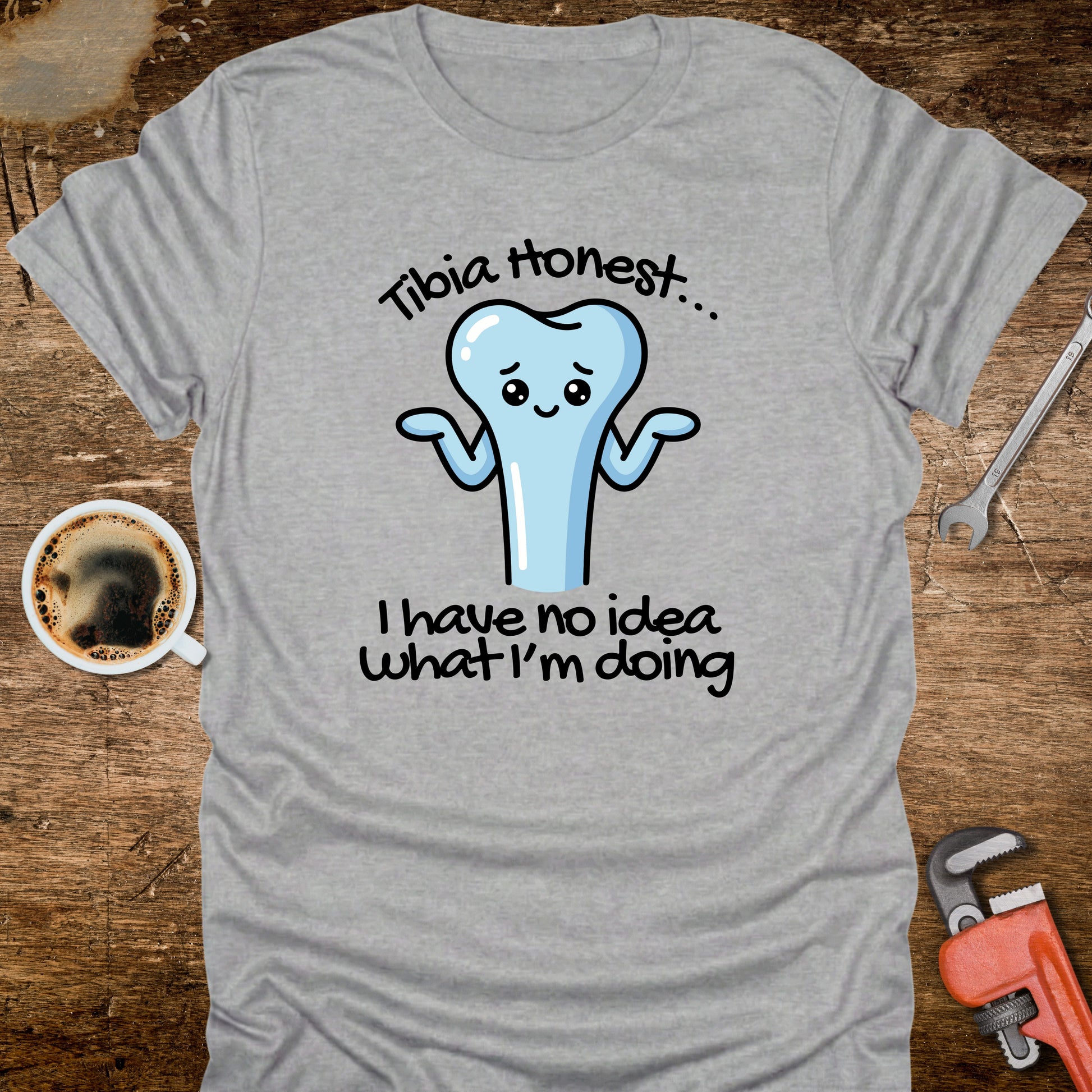 Gray t-shirt with a cartoon tooth graphic and text on a wooden surface with a coffee cup and tools.