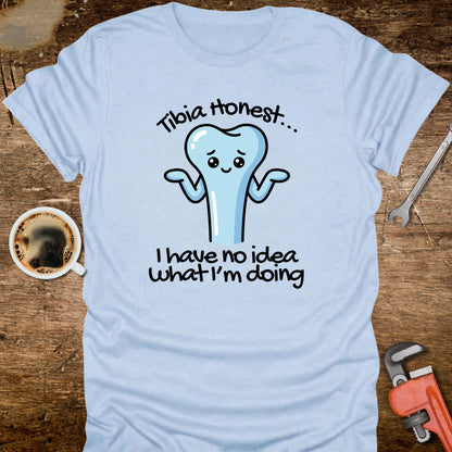 Light blue t-shirt with a cartoon tooth graphic and text on a wooden surface with tools and a coffee cup.