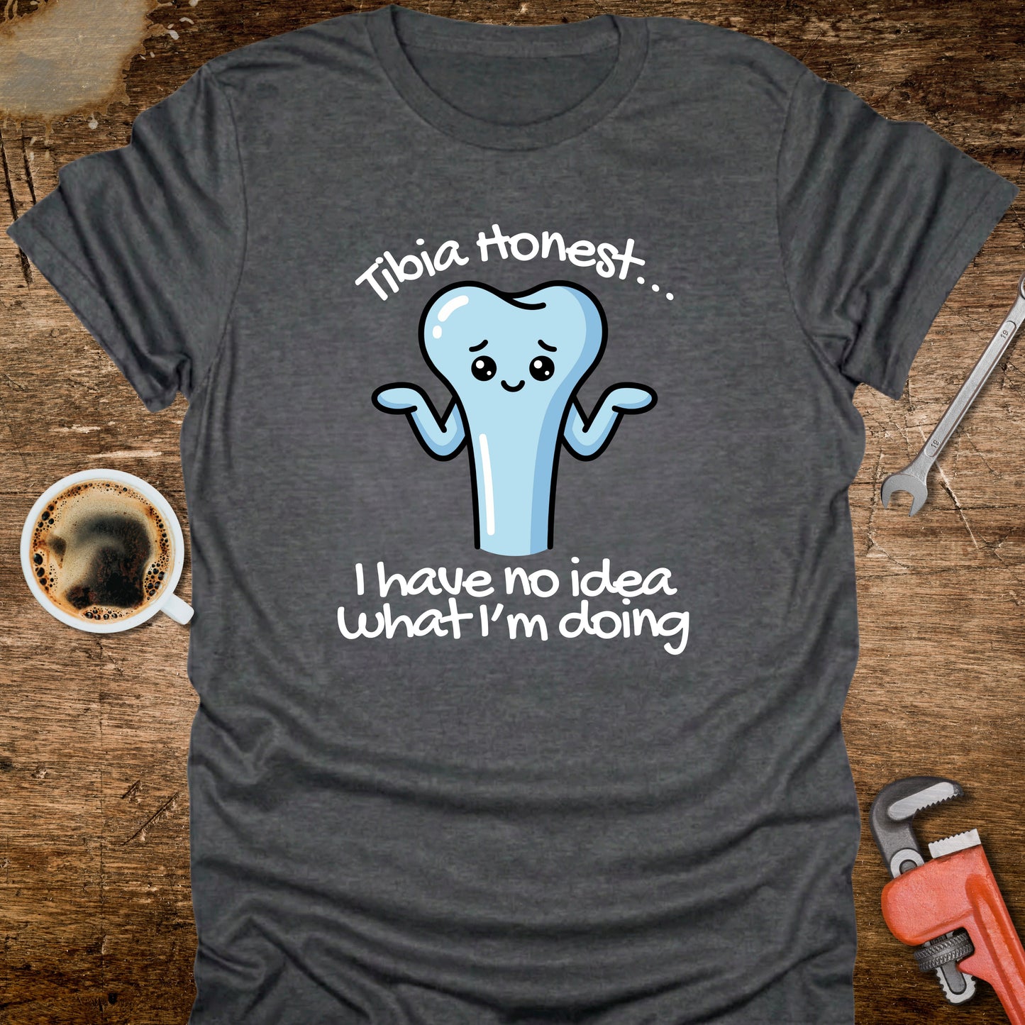 Gray t-shirt with a cartoon tooth graphic and text on a wooden surface with a coffee cup and tools.