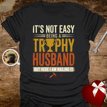 Black t-shirt with humorous text design on a wooden surface with coffee and gift.